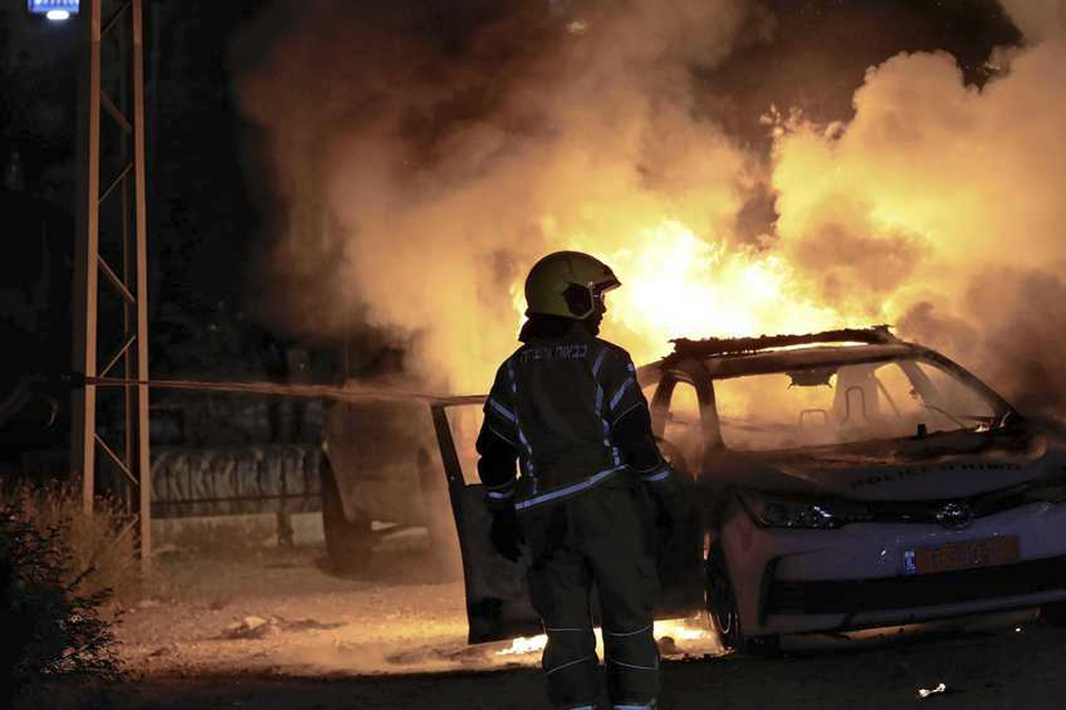 Een brandweerman blust een Israëlische politiewagen die bij de rellen tussen Joden en Arabieren in de stad Lod in de brand werd gestoken. 