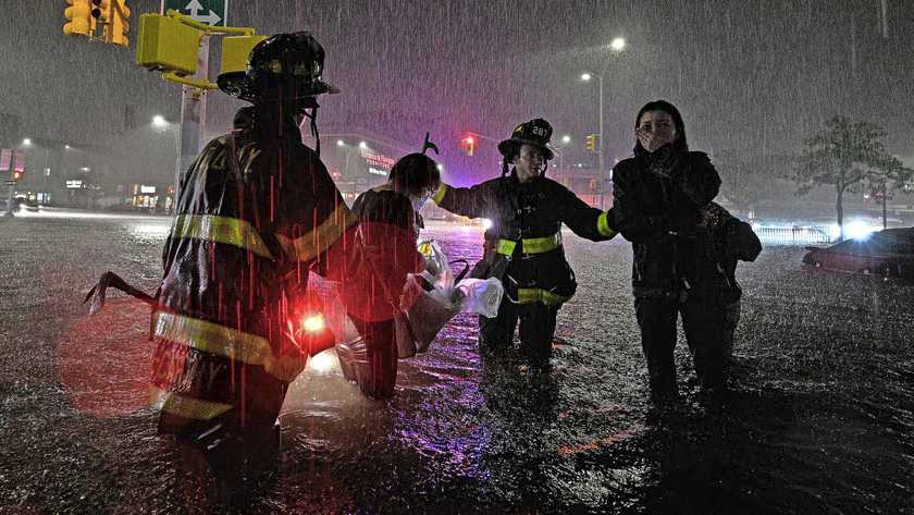 Brandweerlieden helpen vrouw die met haar auto is gestrand door het hoge water. 