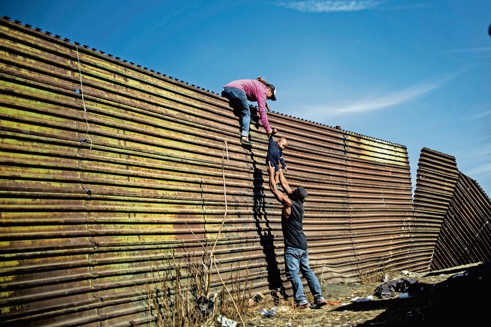 Migranten uit  Latijns-Amerika proberen over een hek te komen aan de grens tussen Mexico en de Verenigde Staten.