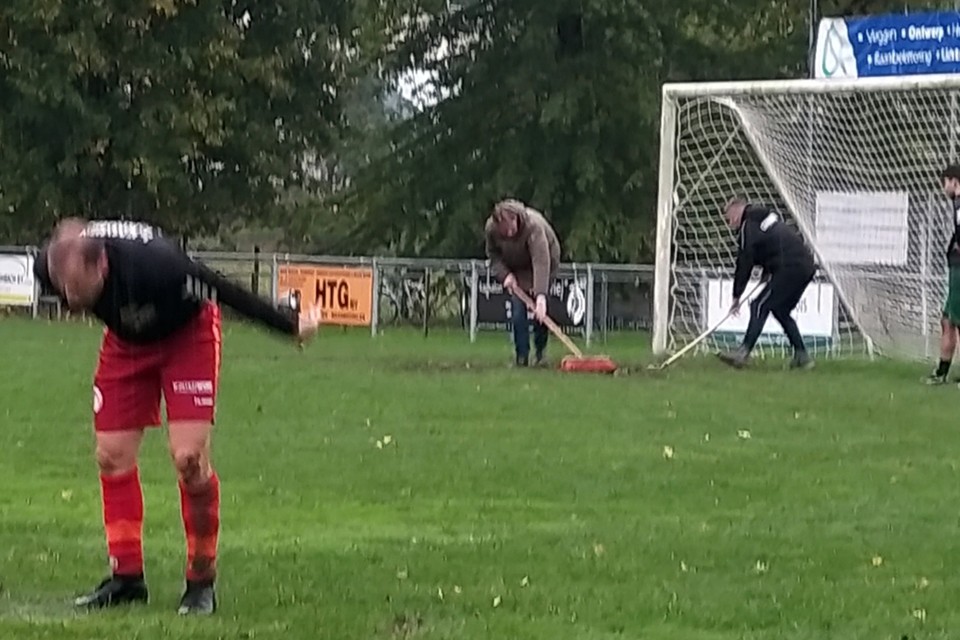 Bestuursleden van SV Geuldal vegen het veld schoon na een hevige regenbui. 