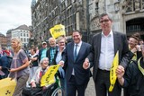 thumbnail: Burgemeester Ralf Krewinkel hand in hand met de burgemeester van Aken, Marcel Philipp, en andere actievoerders voor het raadhuis in Aken. 