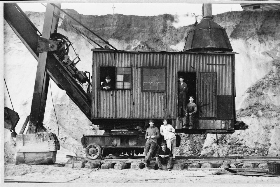 In de bruinkoolgroeve Carisborg I Passart, met machinist Sjeng Meulenberg, staand in de cabine Joep Schneider, zittend stoker Nico Waanders en zittend op de rail Hein Knarren. Overigen zijn niet bekend.