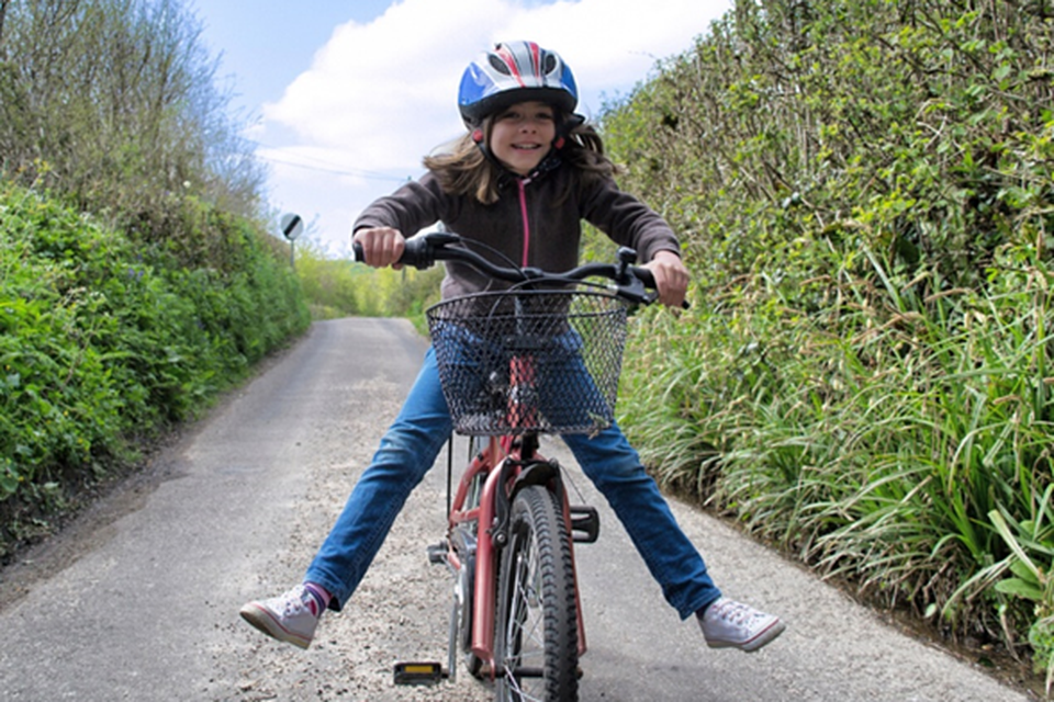 Een meisje met fietshelm vrolijk op haar fiets. Je gunt elk kind toch dit plezier op de pedalen?