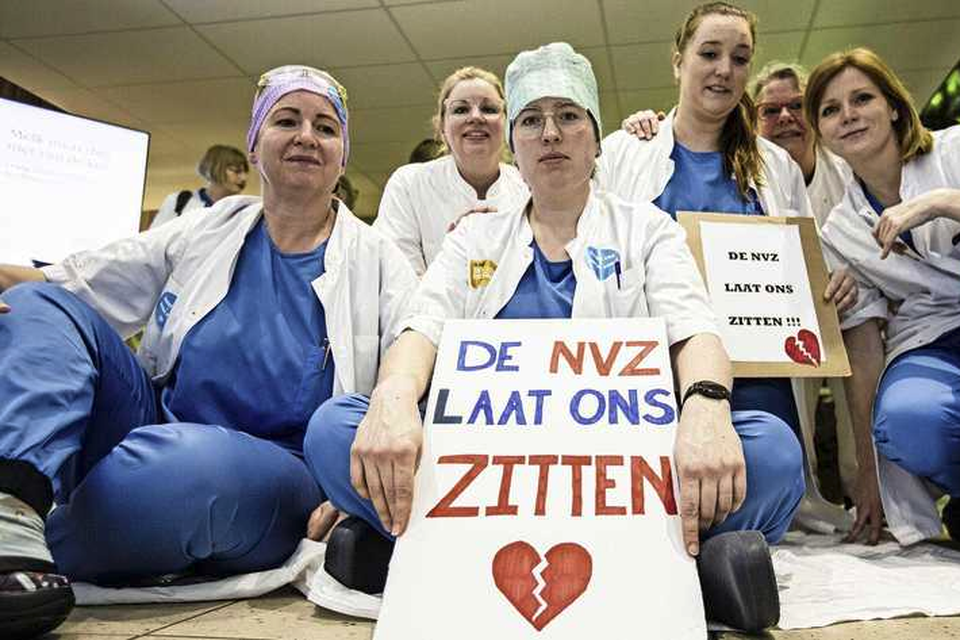 Medewerkers van het Antoni van Leeuwenhoek ziekenhuis in Amsterdam zitten op de grond als actie voor een betere cao.