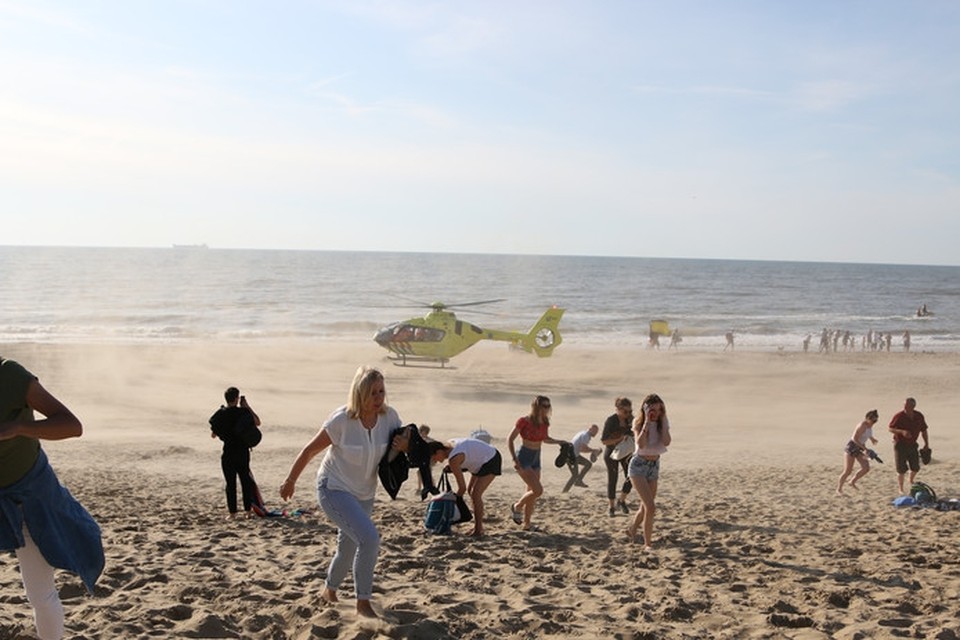 Strandgangers aan de Wassenaarse Slag ontvluchten de zandstorm die een traumahelikopter veroorzaakt die zwemmers in nood komt helpen 