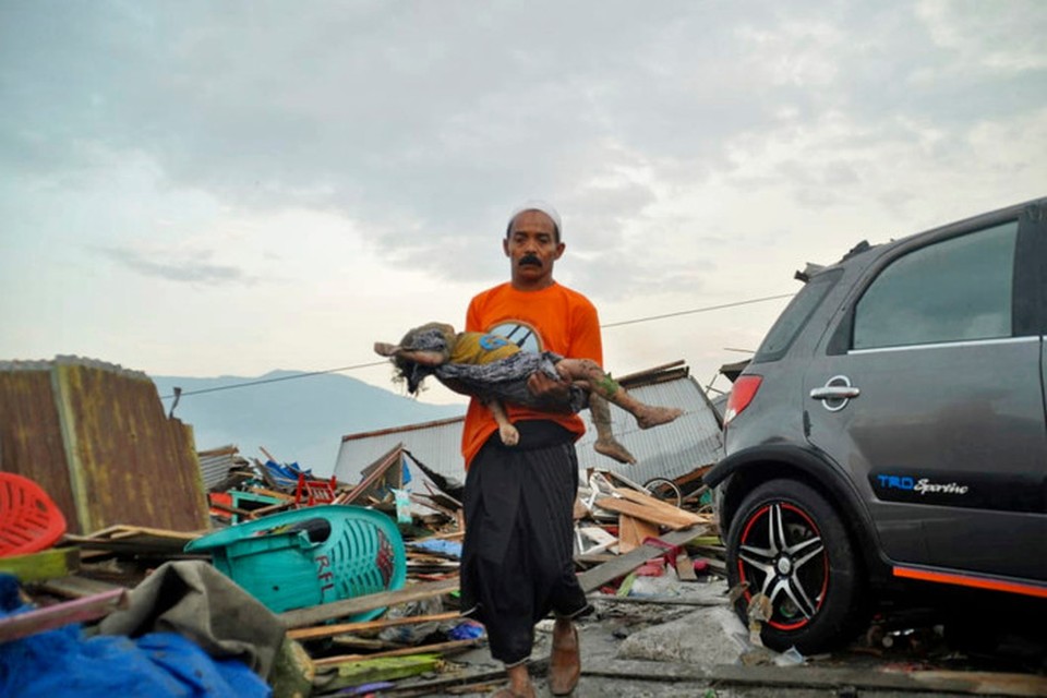 Een man draagt het lichaam van een kind dat overvallen werd door de tsunami in Palu, 