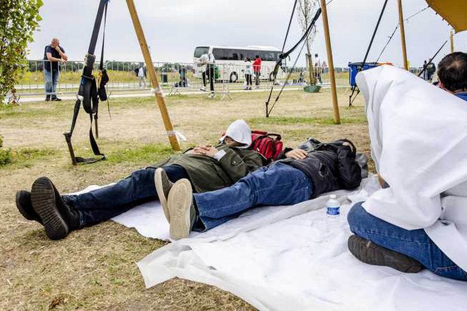 Asielzoekers wachten op een grasveld bij het aanmeldcentrum. Een op de drie medewerkers van het Centraal Orgaan opvang asielzoekers (COA) in Ter Apel zit door een te hoge werkdruk ziek thuis. 