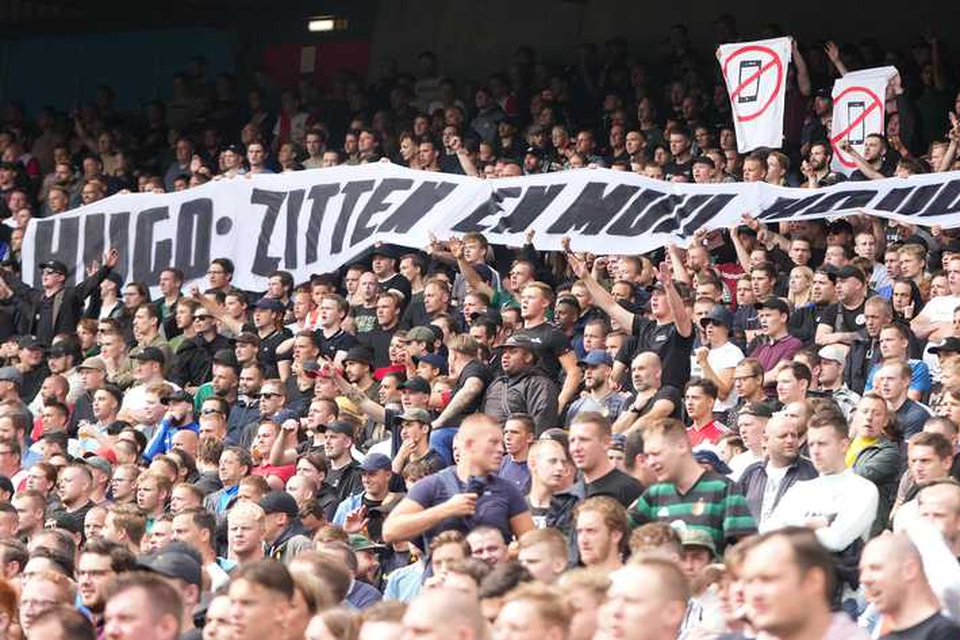 Supporters van Feyenoord houden een spandoek omhoog met de tekst: ’Hugo: zitten en muil houden’. 
