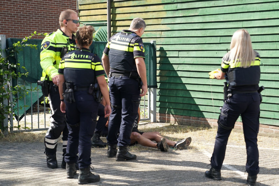 Politiemensen rond de verwarde man die op de grond zit. 