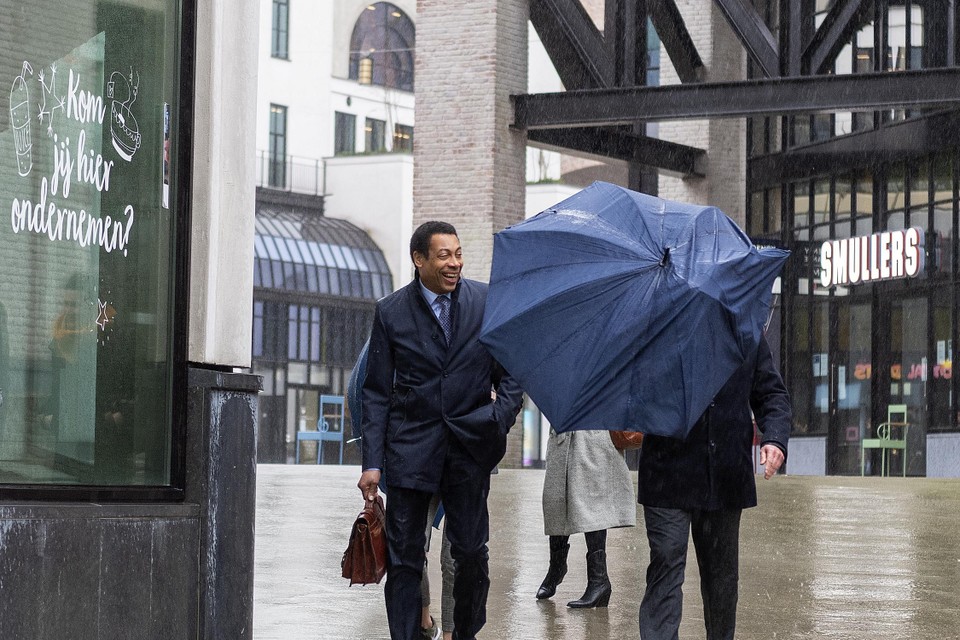 Minister Franc Weerwind lacht bij zijn aankomst in Heerlen als burgemeester Roel Wever door een windvlaag achter zijn paraplu verdwijnt.