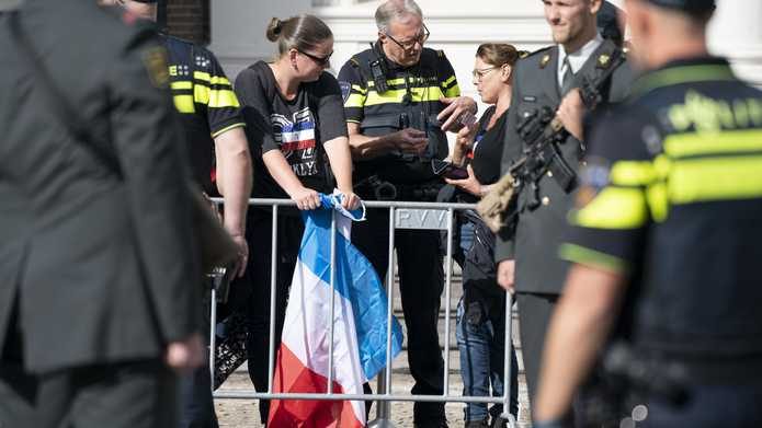 Politieagenten praten met toeschouwers met een omgekeerde Nederlandse vlag langs de route op Prinsjesdag. 