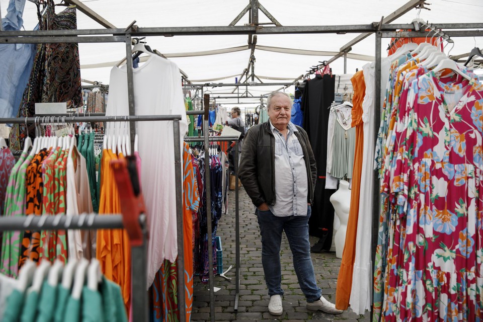 Ton Schäfer in zijn marktkraam vol kleurrijke kleding. 