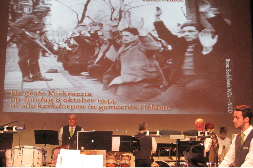 Een beeld van het concert uit de film met op het grote scherm de grote Kerkrazzia van 8 oktober 1944. 