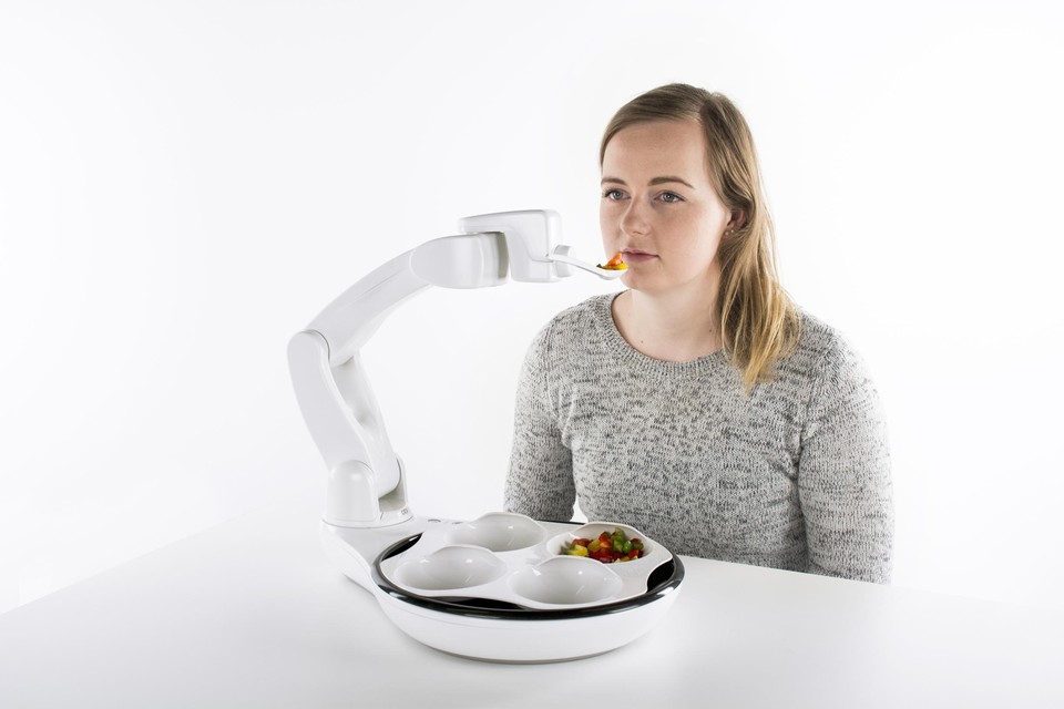 Een medewerkster van een bedrijf toont een robot die helpt mensen, die dat niet meer kunnen,  zelfstandig te  eten 